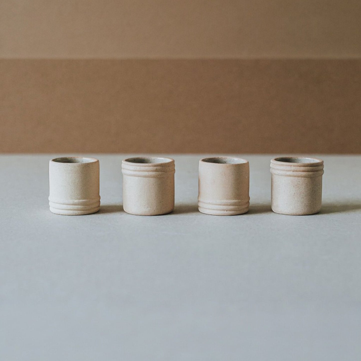Artisan ceramic tequila and mezcal shot glasses in light sand tone displayed in a clean minimal setting