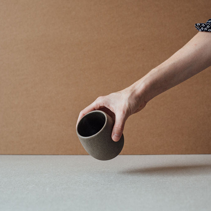Hand tilting a chocolate-tone round ceramic cup to show its interior.