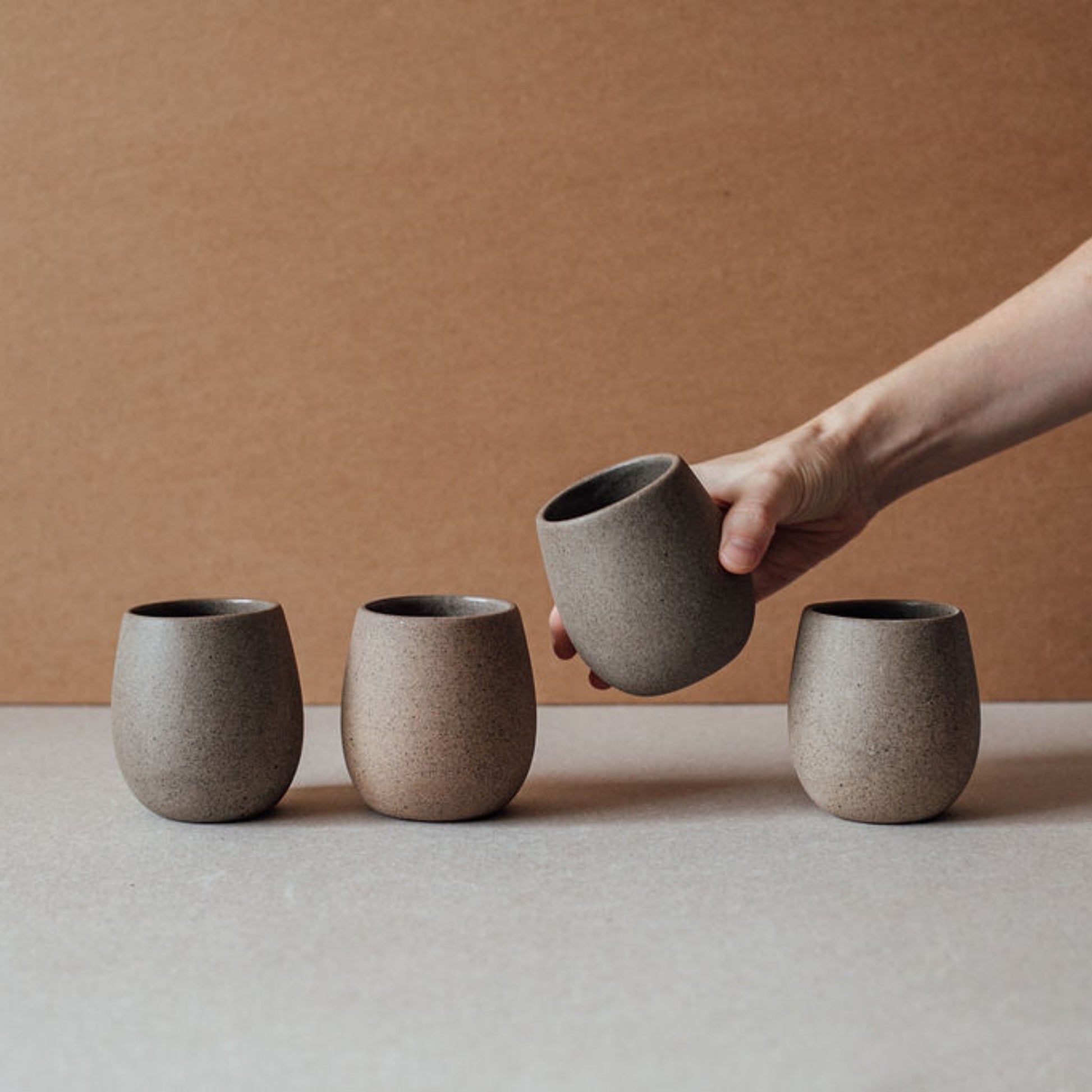 Hand lifting a rounded ceramic cup while three others stand in a row.