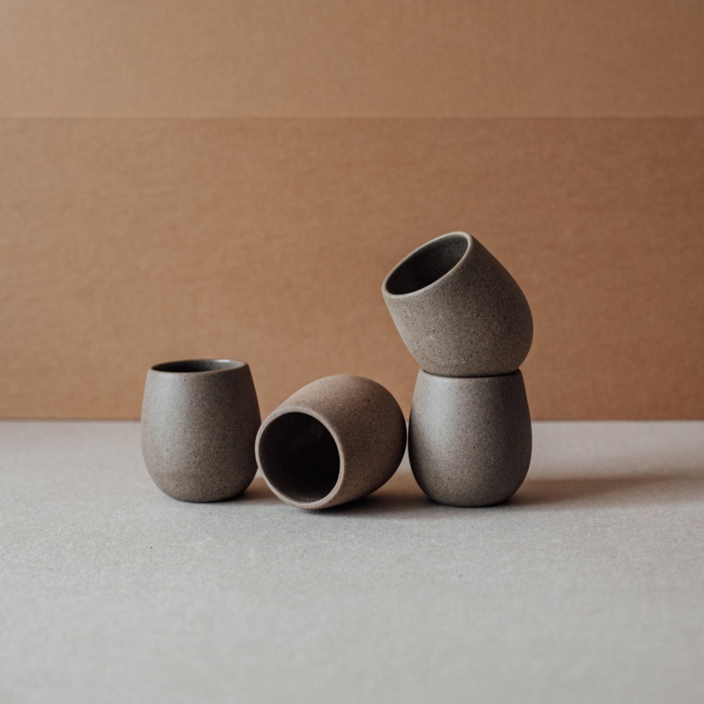 Four round ceramic cups in chocolate tone arranged on a neutral background.