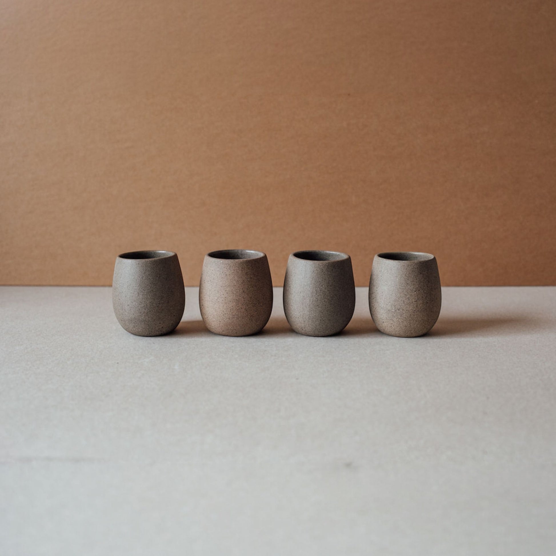 Four round ceramic cups in warm chocolate colors lined up on a neutral surface.