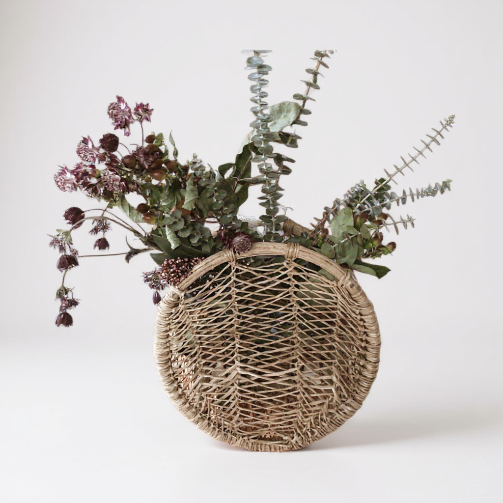 Handwoven circular jonote basket filled with dried flowers on a white background.