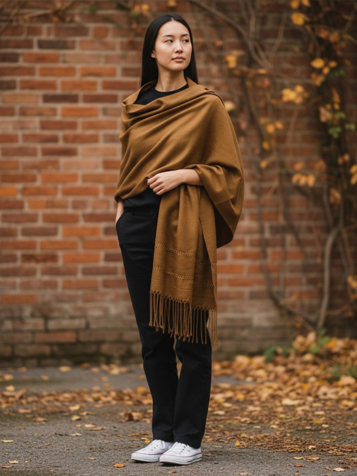 Woman wearing a handwoven silk-blend rebozo shawl in golden, standing against a brick wall