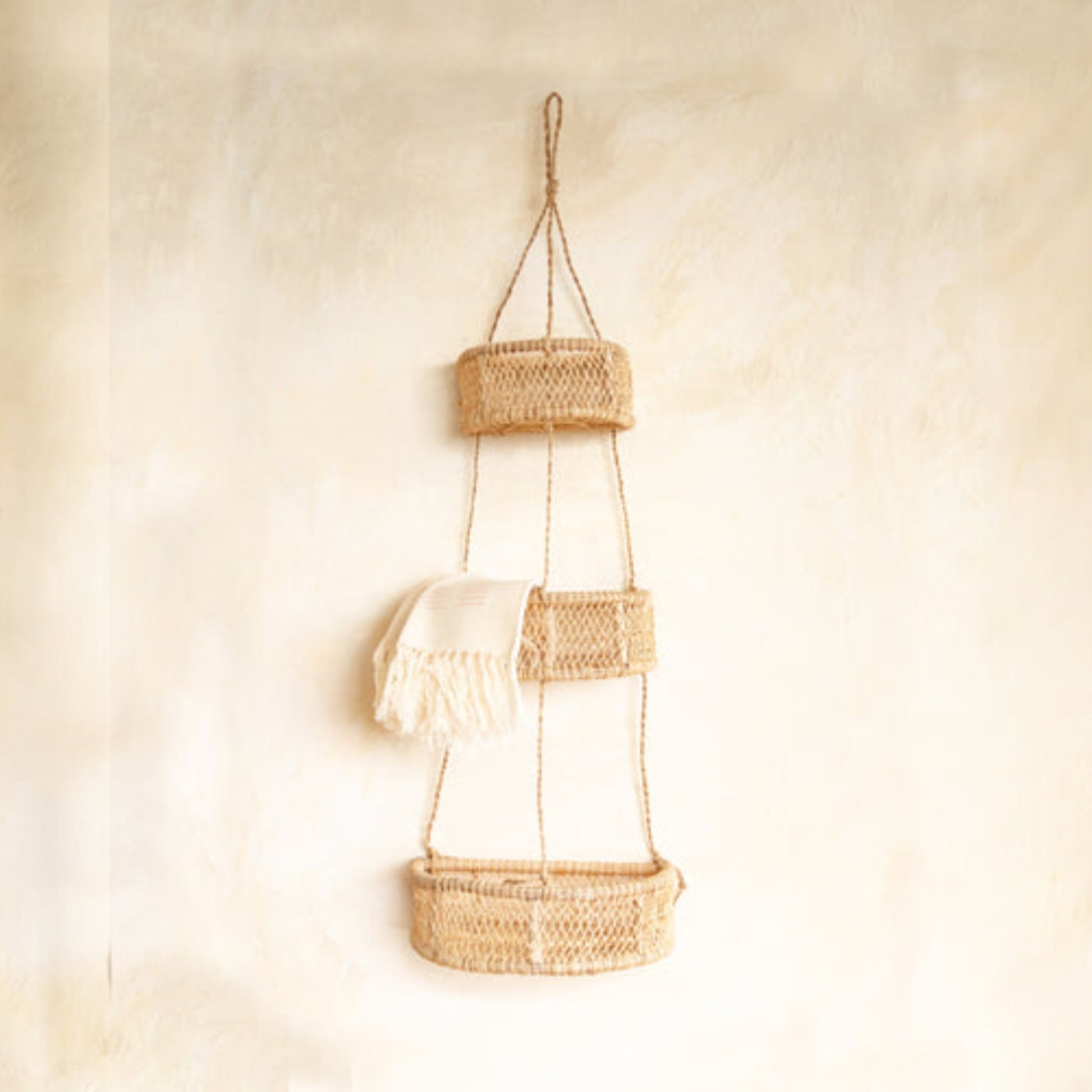 Three-tier woven hanging basket with a white cloth on a beige textured wall