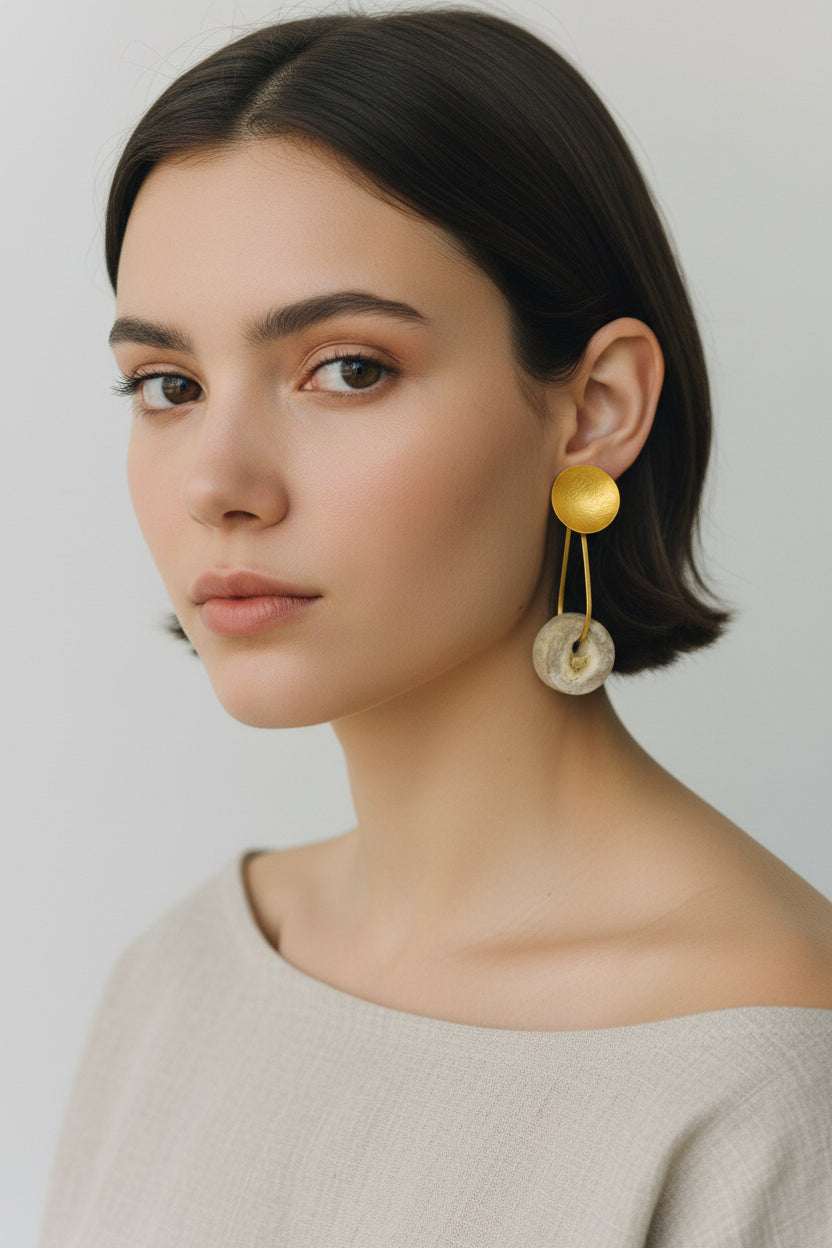 Woman wearing gold horn disc drop earrings, front portrait with neutral background and soft natural light