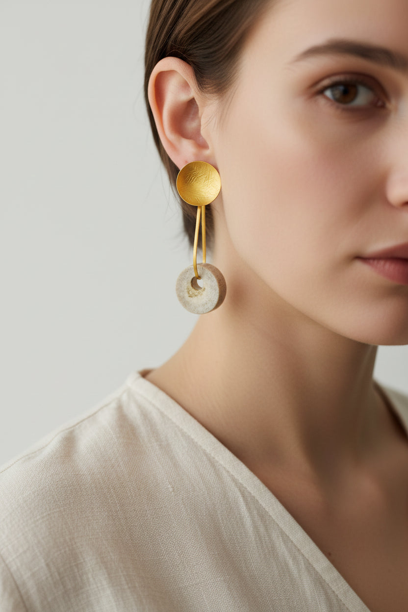 Woman wearing gold horn disc drop earrings, side view highlighting elongated sculptural drop design