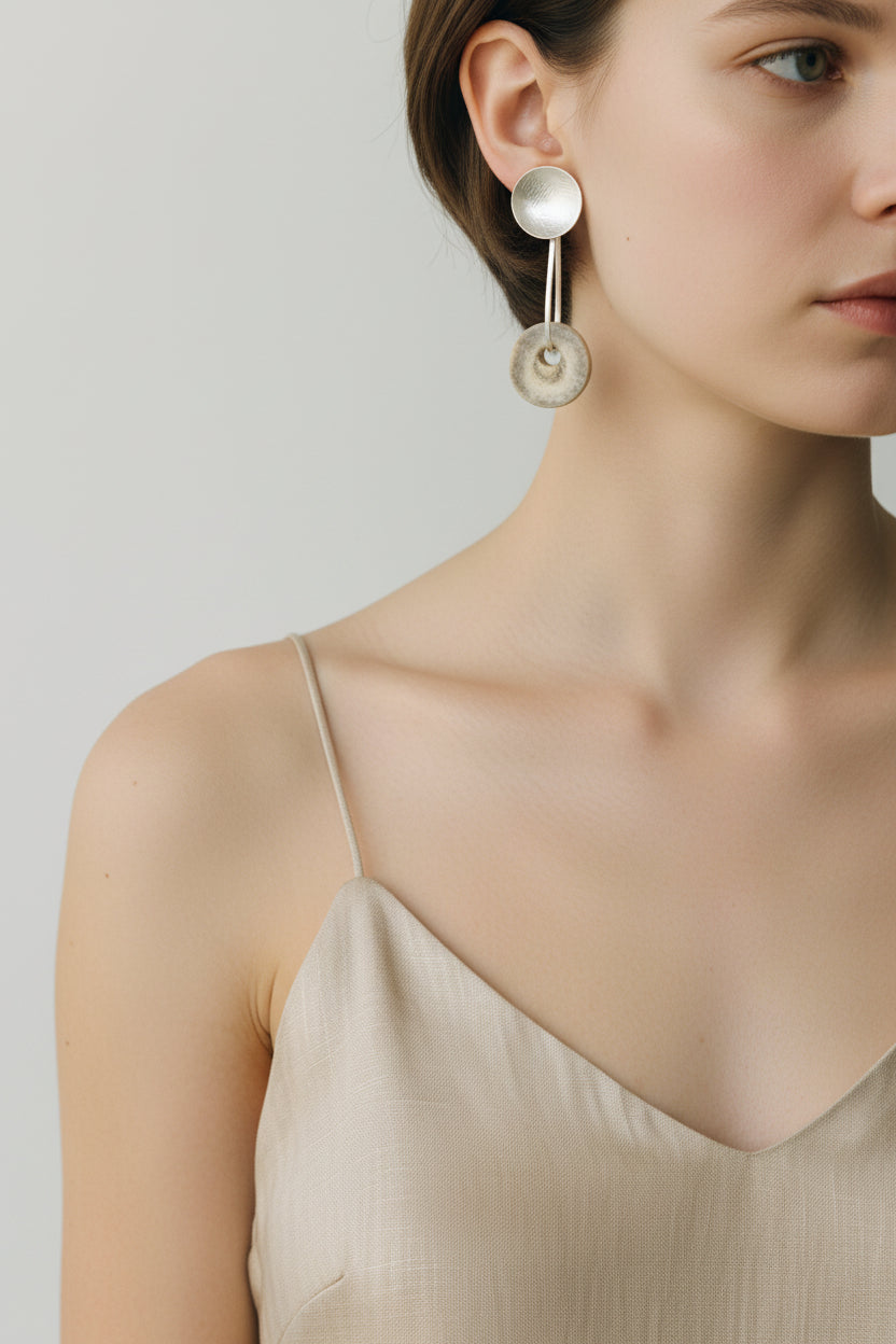 Woman wearing silver horn disc drop earrings, close-up portrait with hair pulled back and soft lighting