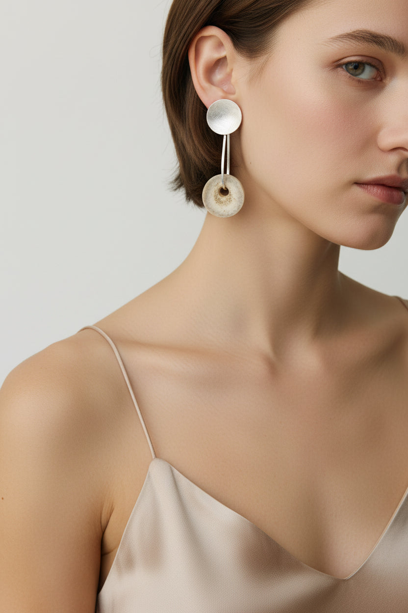 Woman wearing gold horn disc drop earrings, three-quarter profile showing sculptural metal disc and natural antler drop
