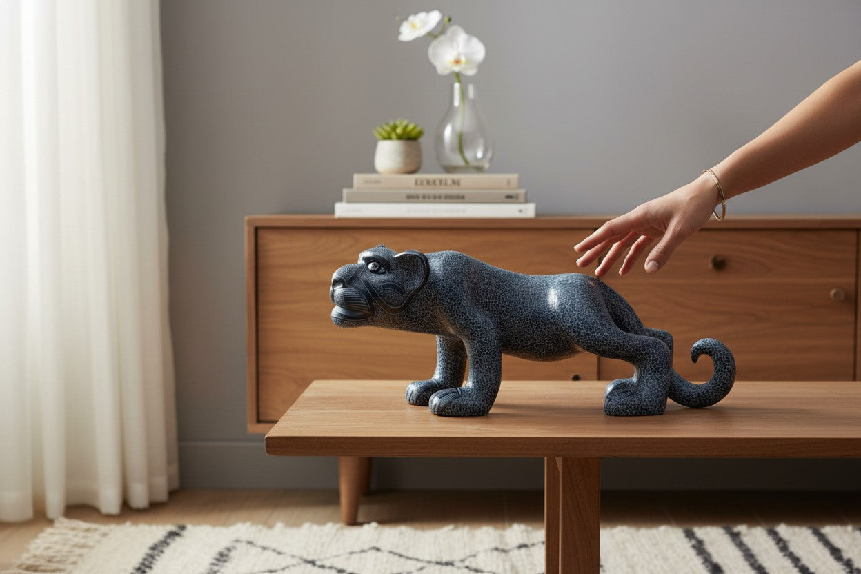 A hand-painted black ceramic reclining Mayan jaguar sculpture displayed on a light wood table with a hand showing its scale.