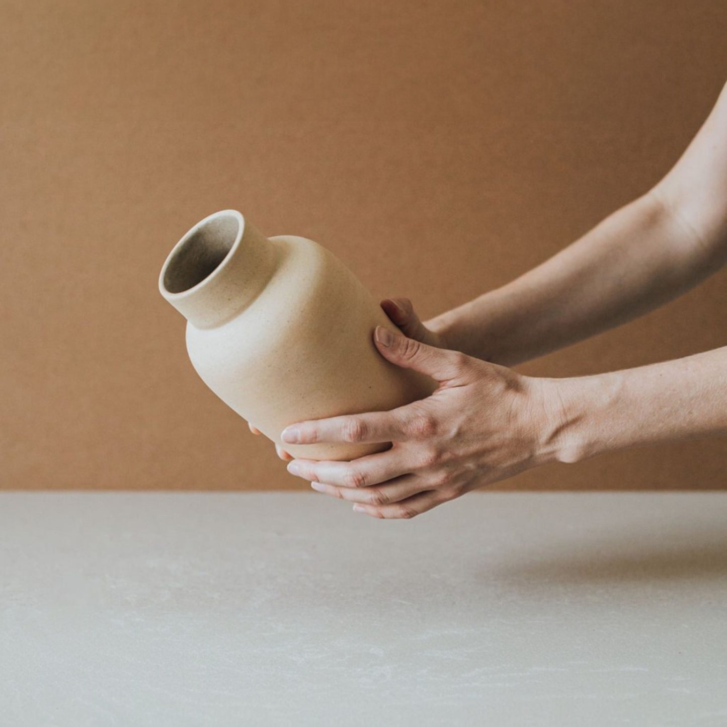 Hand placing a sand terracotta vase, showing its smooth unglazed finish.