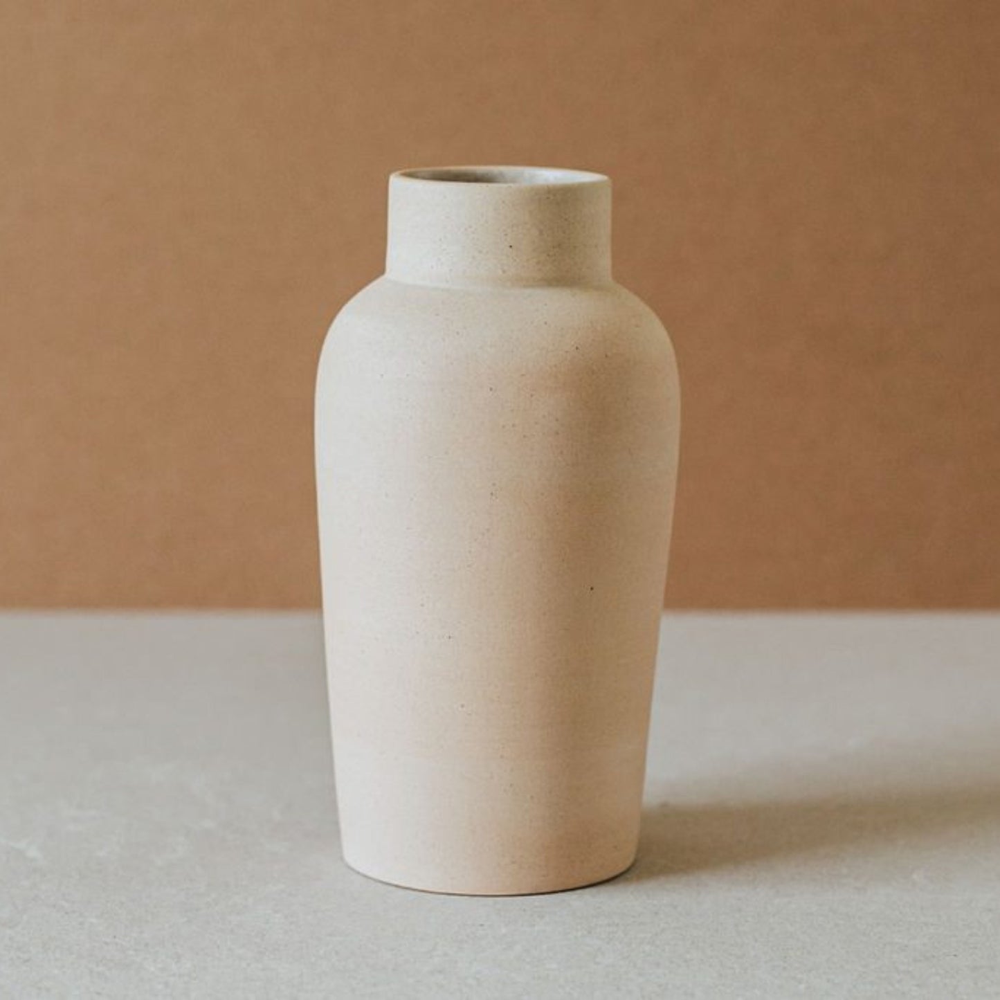 Minimalist bottle-shaped terracotta vase against a warm beige background.