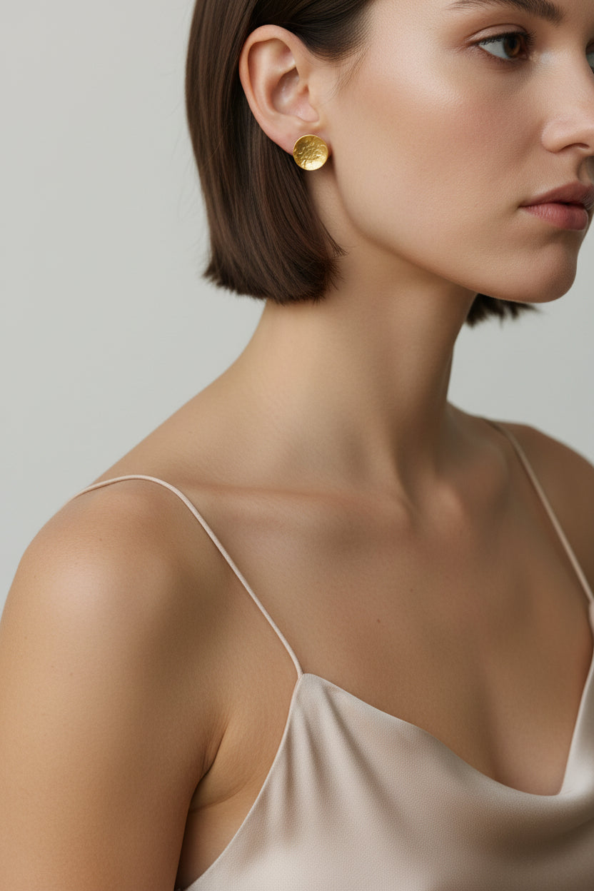 Handmade gold dome stud earrings worn by a woman against a neutral background