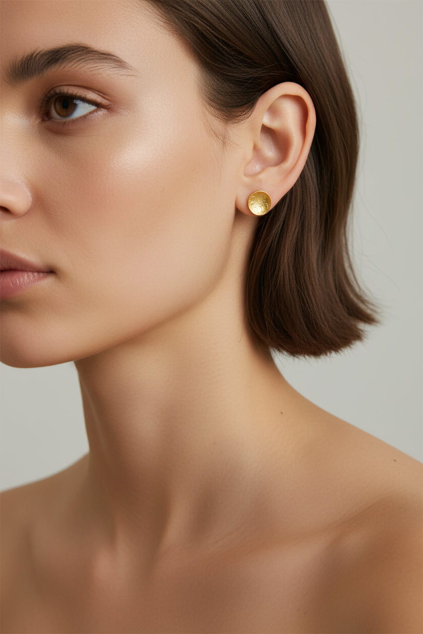 Handmade gold dome stud earrings worn by a woman against a neutral background