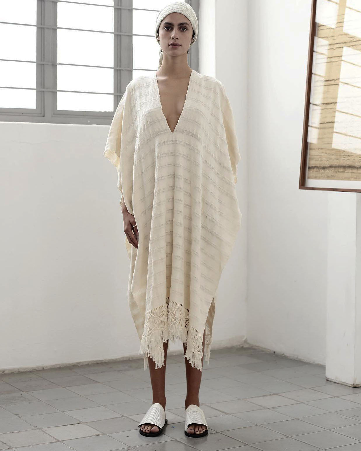 Woman wearing a handwoven cotton poncho dress with deep V-neck and fringe hem, photographed indoors