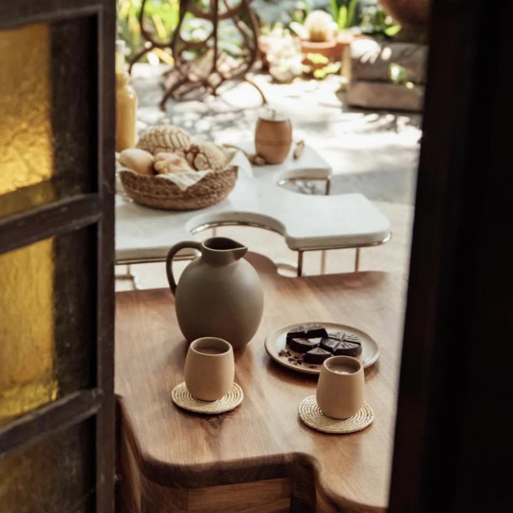 Sculptural terracotta pitcher styled on wooden table with clay cups