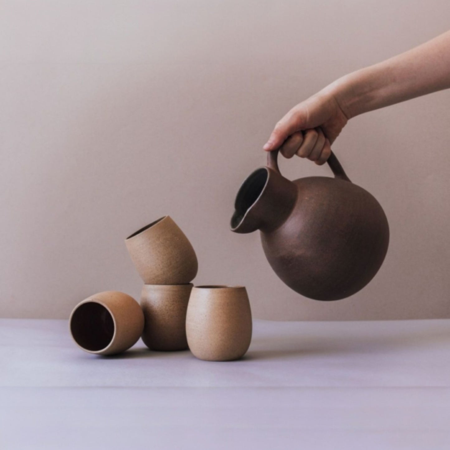 Round terracotta ceramic jug with matching clay cups in earthy tones