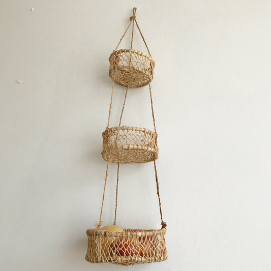 Three-tier hanging circular basket made of jonote fiber against a white wall.