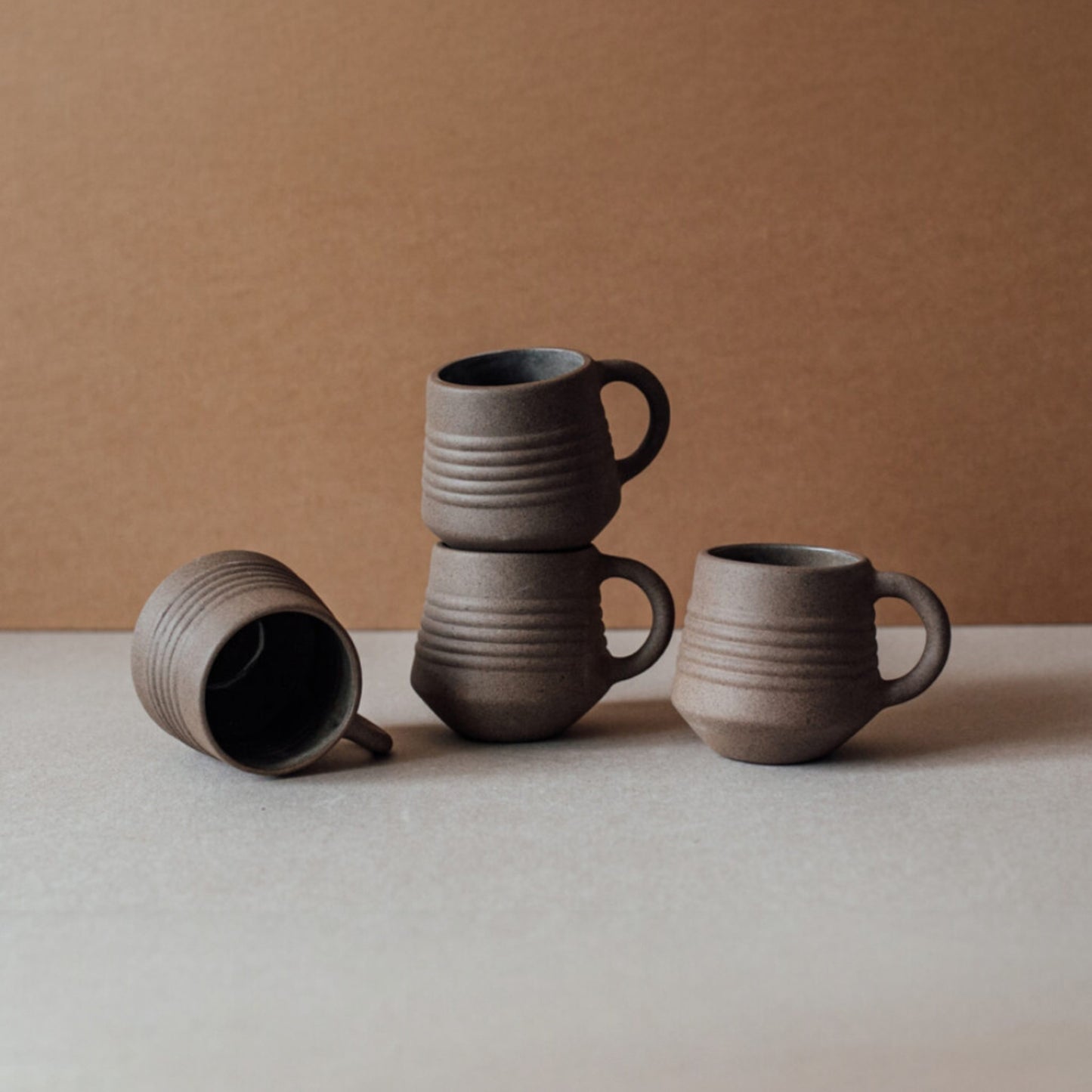 Ridge terracotta coffee mug set stacked with matching ceramic cups in earthy brown tones on neutral background