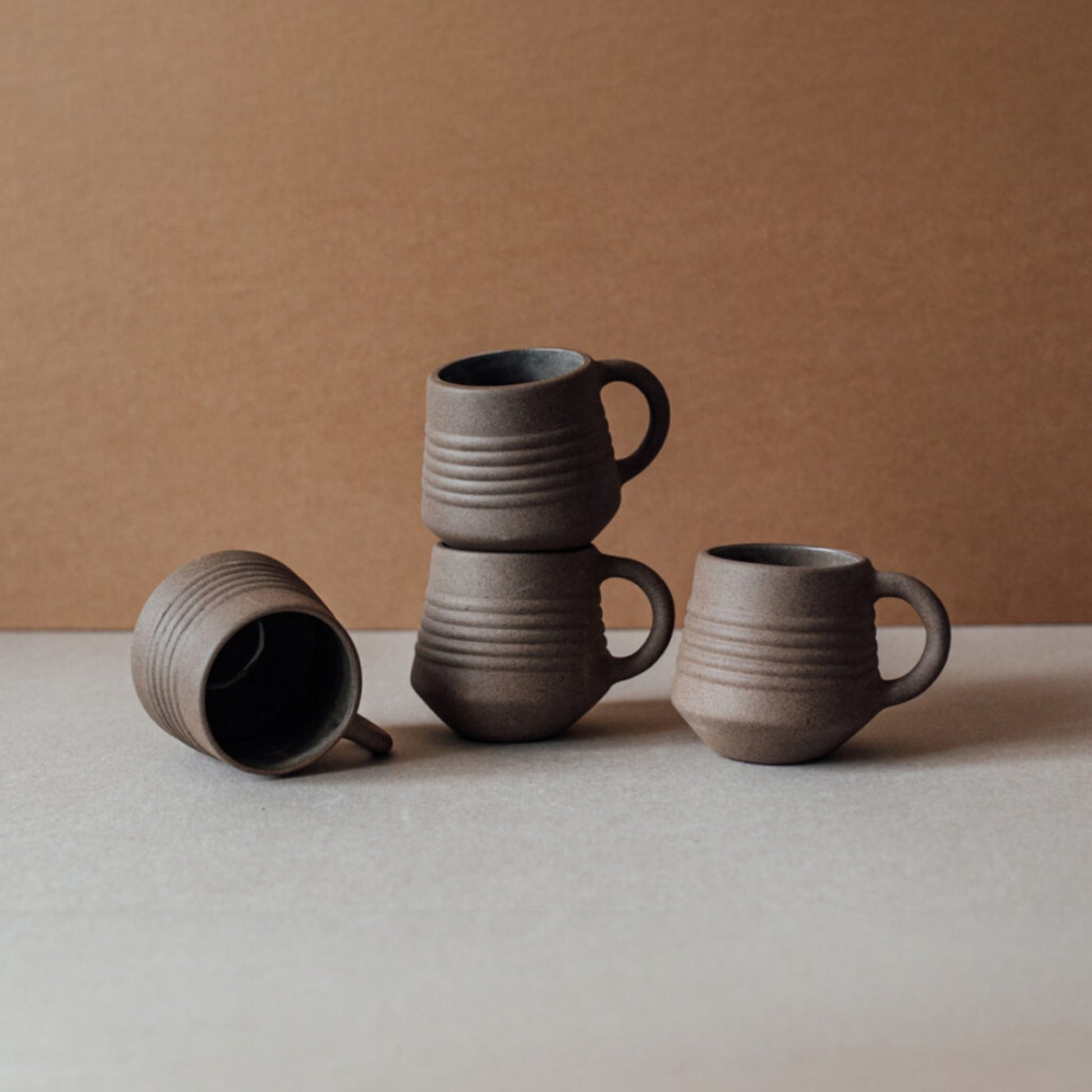 Ridge terracotta coffee mug set stacked with matching ceramic cups in earthy brown tones on neutral background