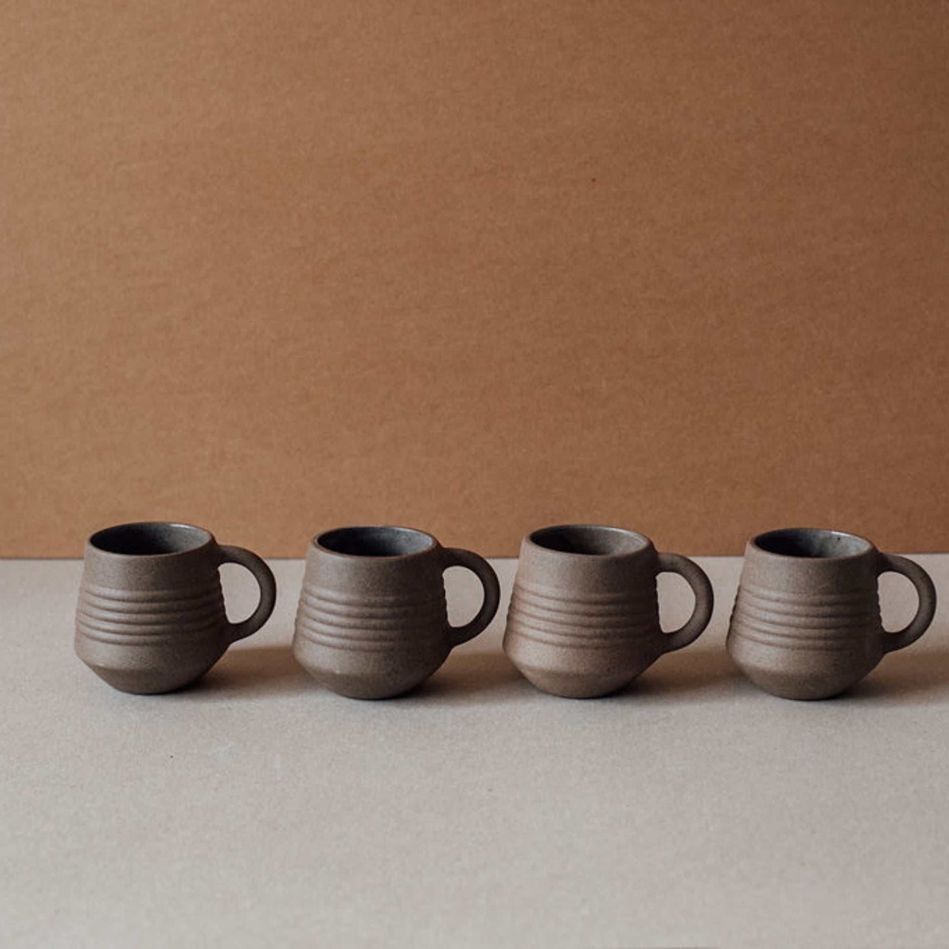 Four ridge terracotta mugs aligned in a row, minimalist ceramic coffee cups in matte earthy finish