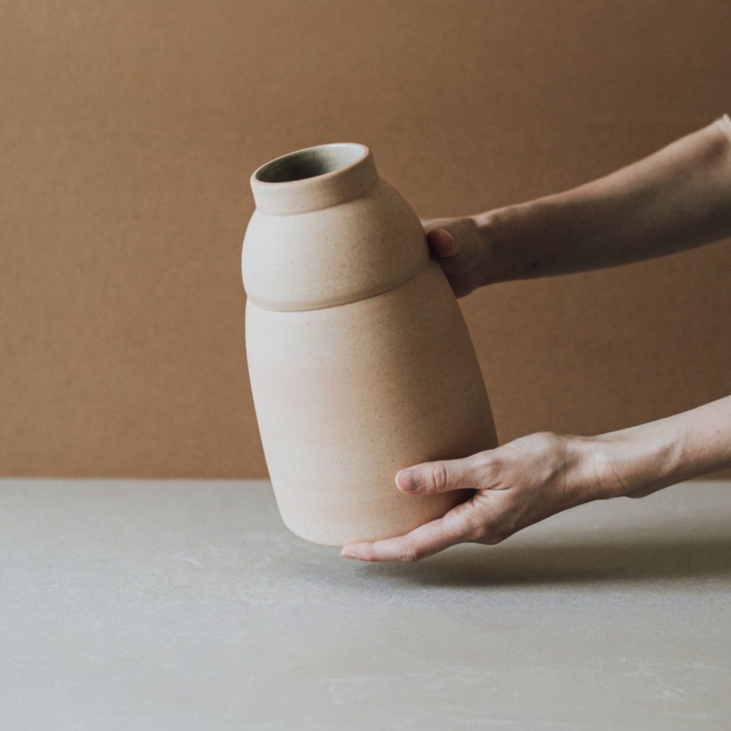 Hand positioning rounded ceramic vase highlighting smooth curves and light clay texture
