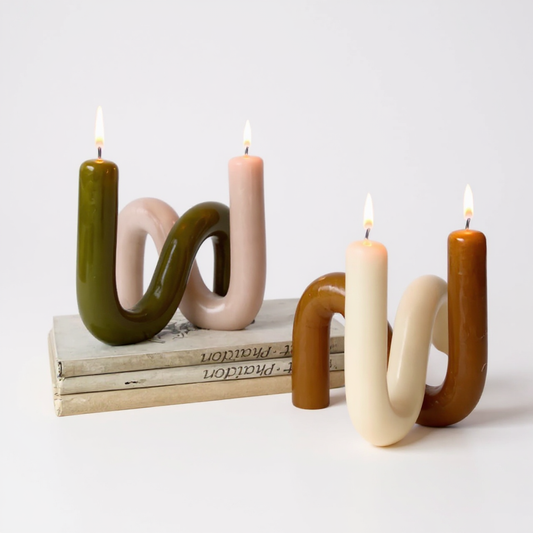 S-shaped sculptural beeswax candles in earthy colors displayed on stacked books