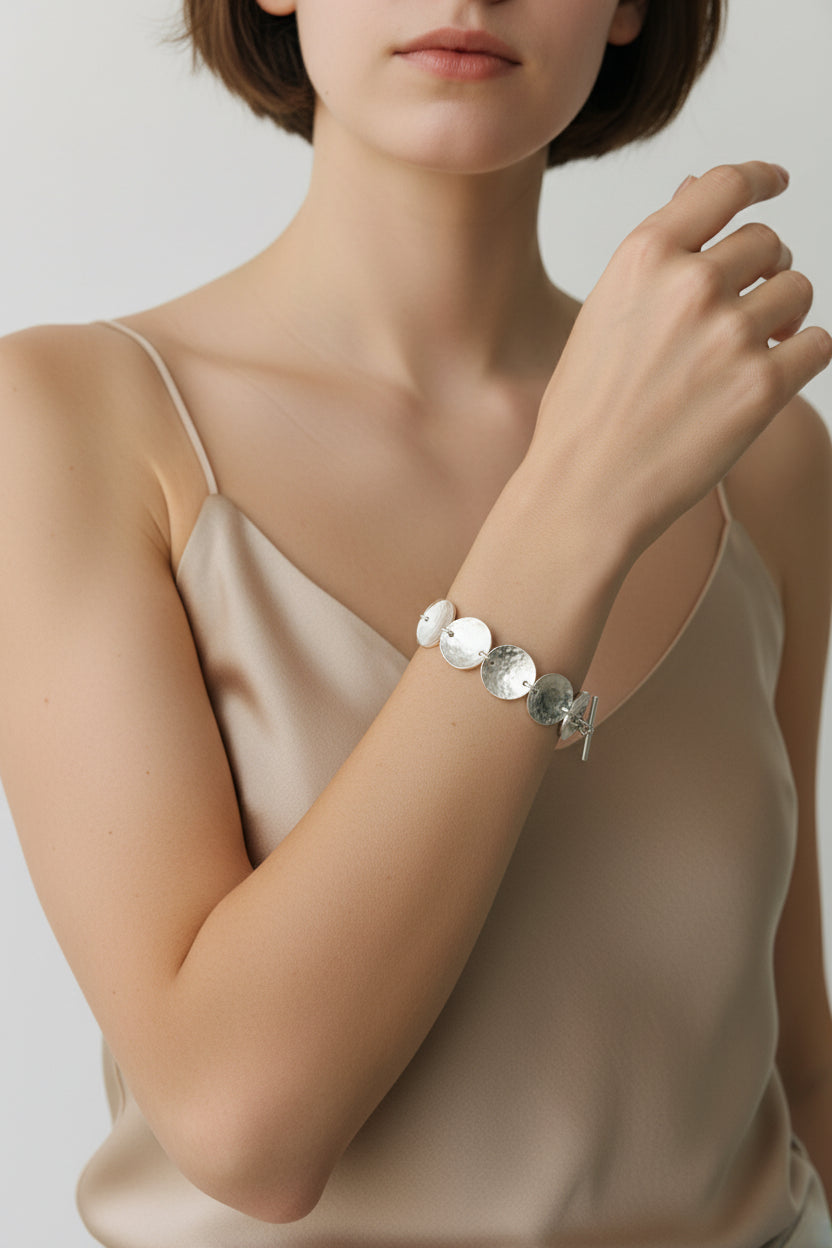 Model wearing sculpted disc bracelet in sterling silver, minimalist neutral background