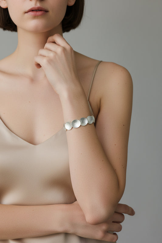 Model wearing sculpted disc bracelet in sterling silver, minimalist neutral background