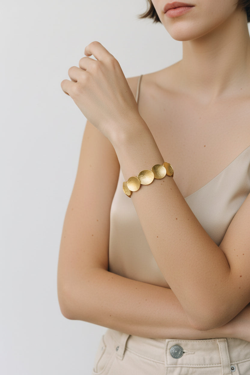 Gold sculpted disc cuff bracelet worn on wrist, editorial pose
