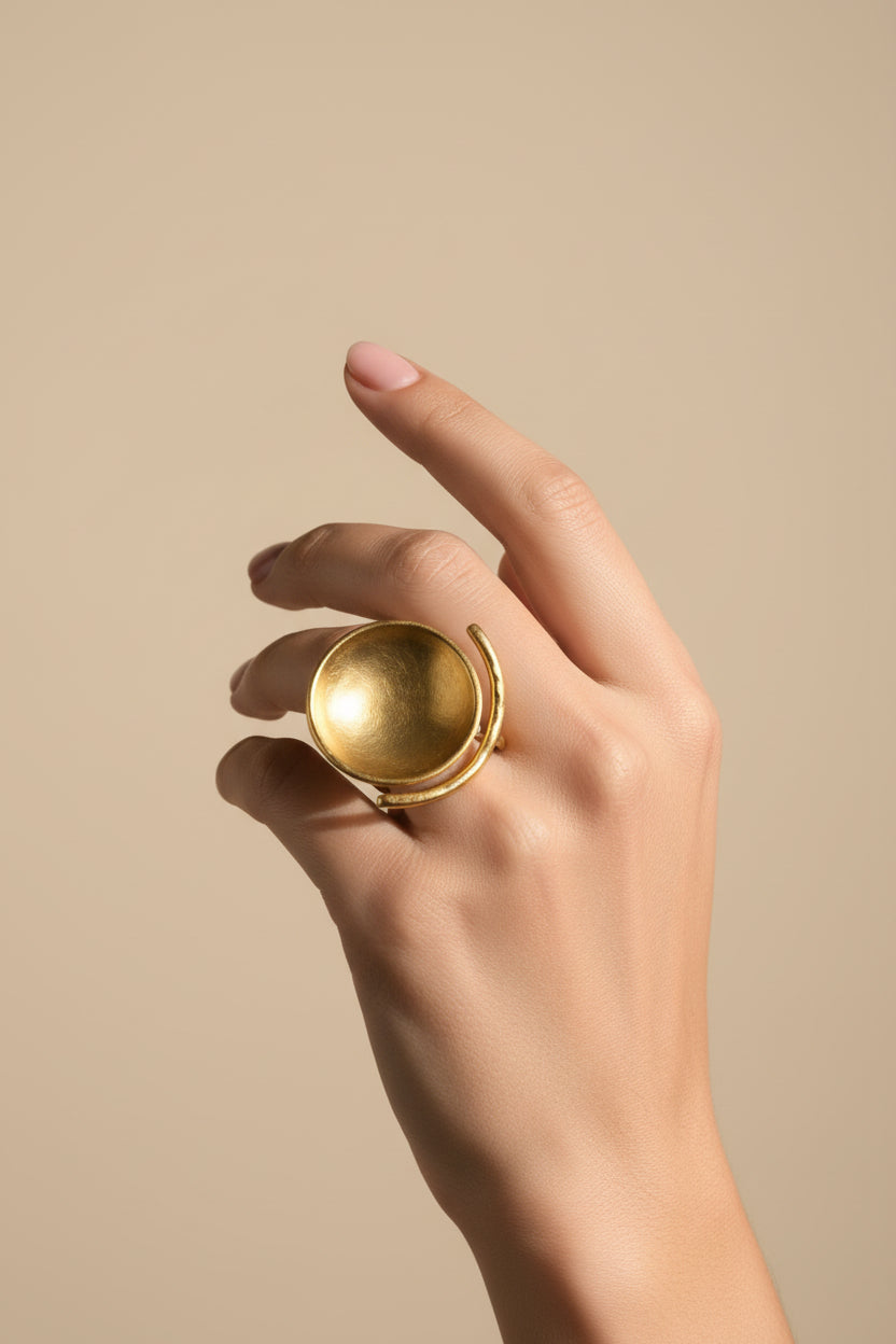 Hand wearing gold sculptural bowl adjustable ring, minimalist studio lighting
