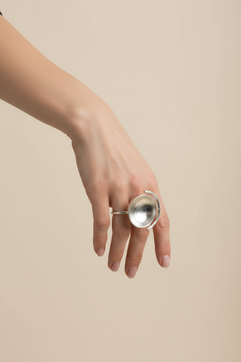 Hand wearing silver sculptural bowl adjustable ring, clean neutral background
