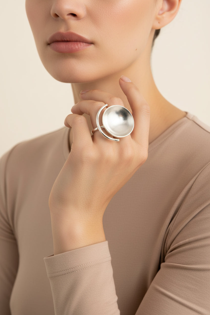 Model wearing sculptural bowl statement ring in silver finish, minimal studio background