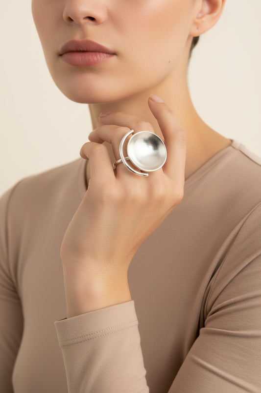 Model wearing sculptural bowl statement ring in silver finish, minimal studio background