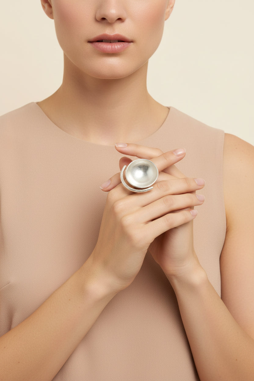 Model wearing silver sculptural bowl statement ring on hand, clean beige background