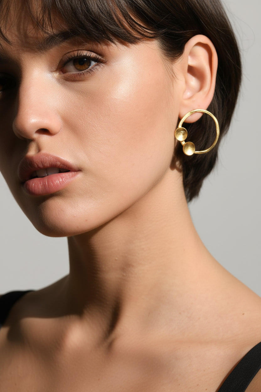 Woman wearing sculptural minimalist gold hoop earrings, close-up