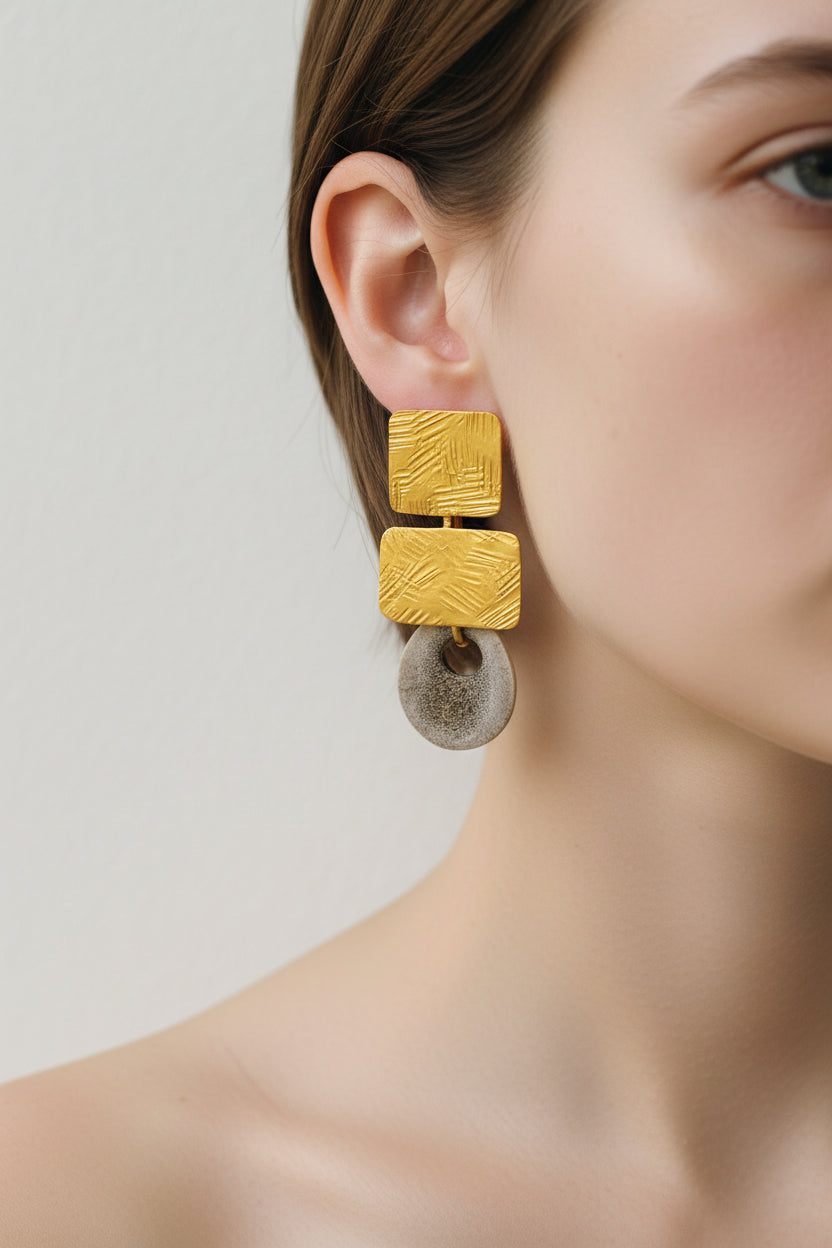 Close-up of model wearing gold square deer horn drop earrings, bare shoulder and natural skin