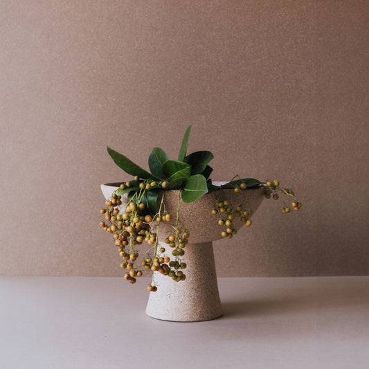 Tall terracotta pedestal bowl with green foliage arranged as a sculptural table centerpiece
