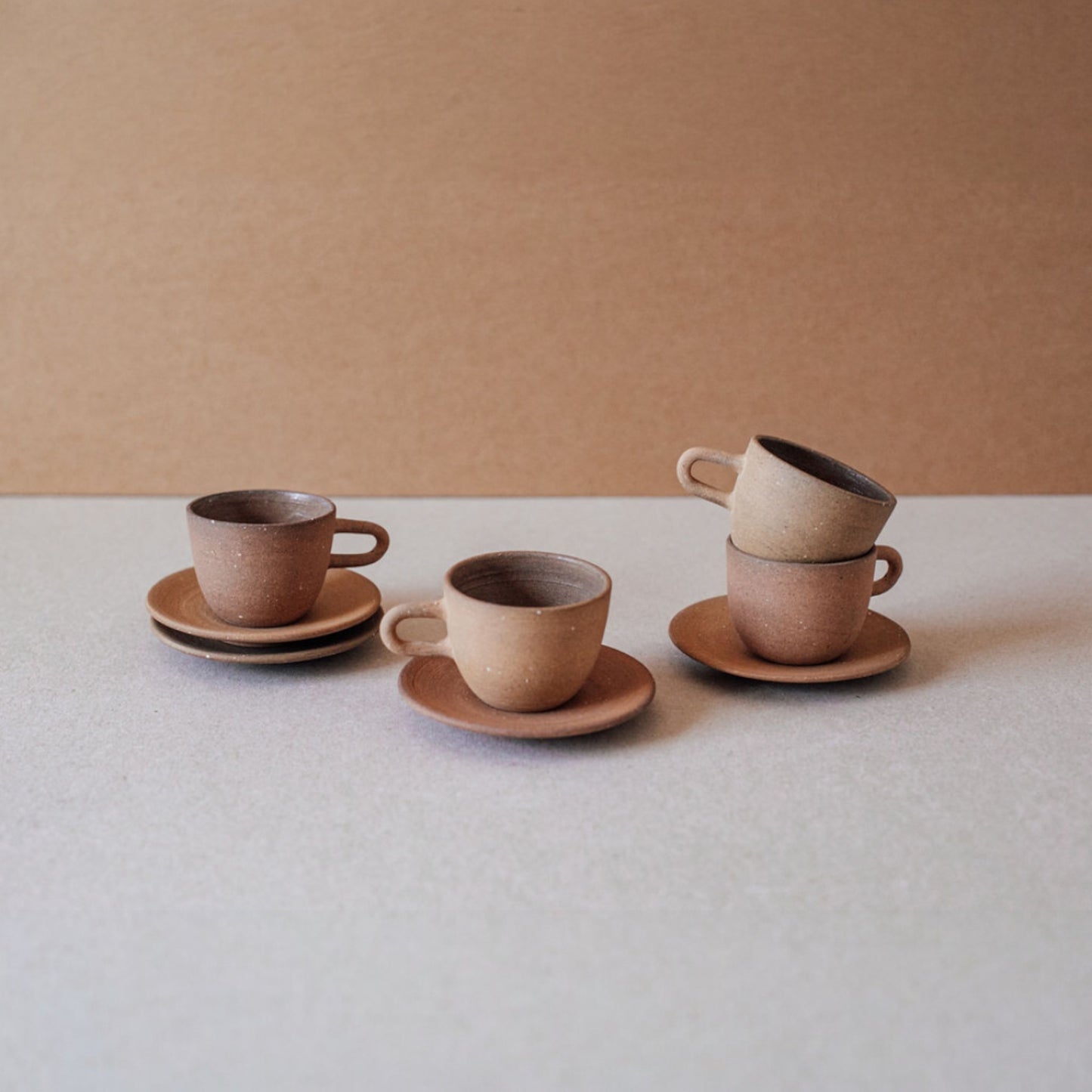 Stacked terracotta espresso cups with saucers on neutral background