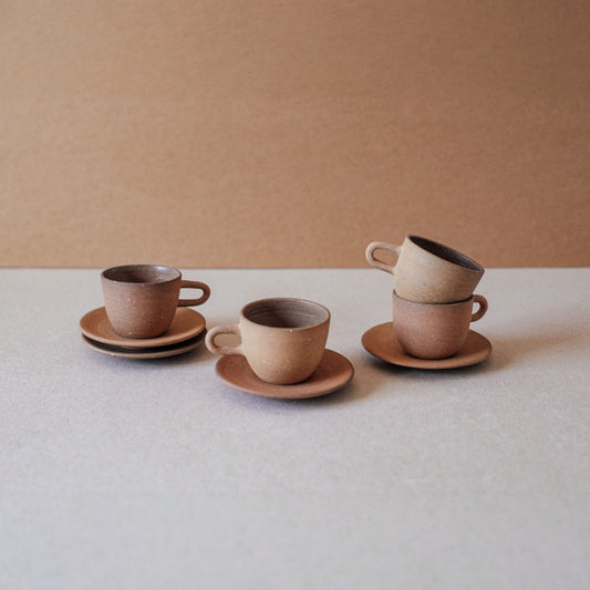 Stacked terracotta espresso cups with saucers on neutral background
