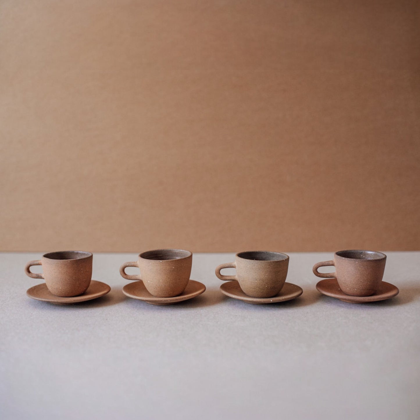 Four ceramic espresso cups with saucers in terracotta tones