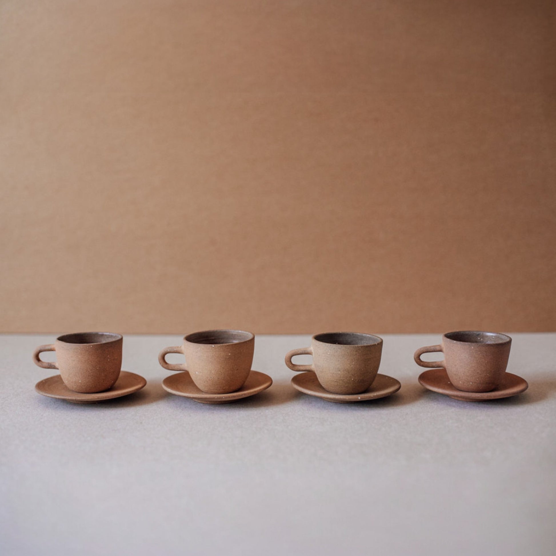 Four ceramic espresso cups with saucers in terracotta tones