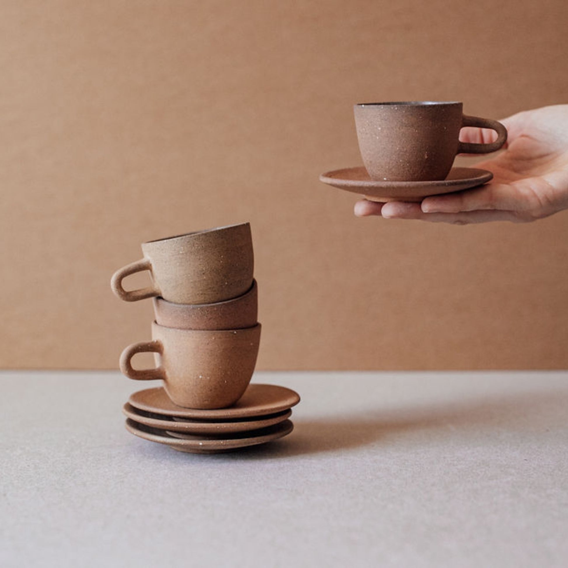Hand holding terracotta espresso cup with saucer