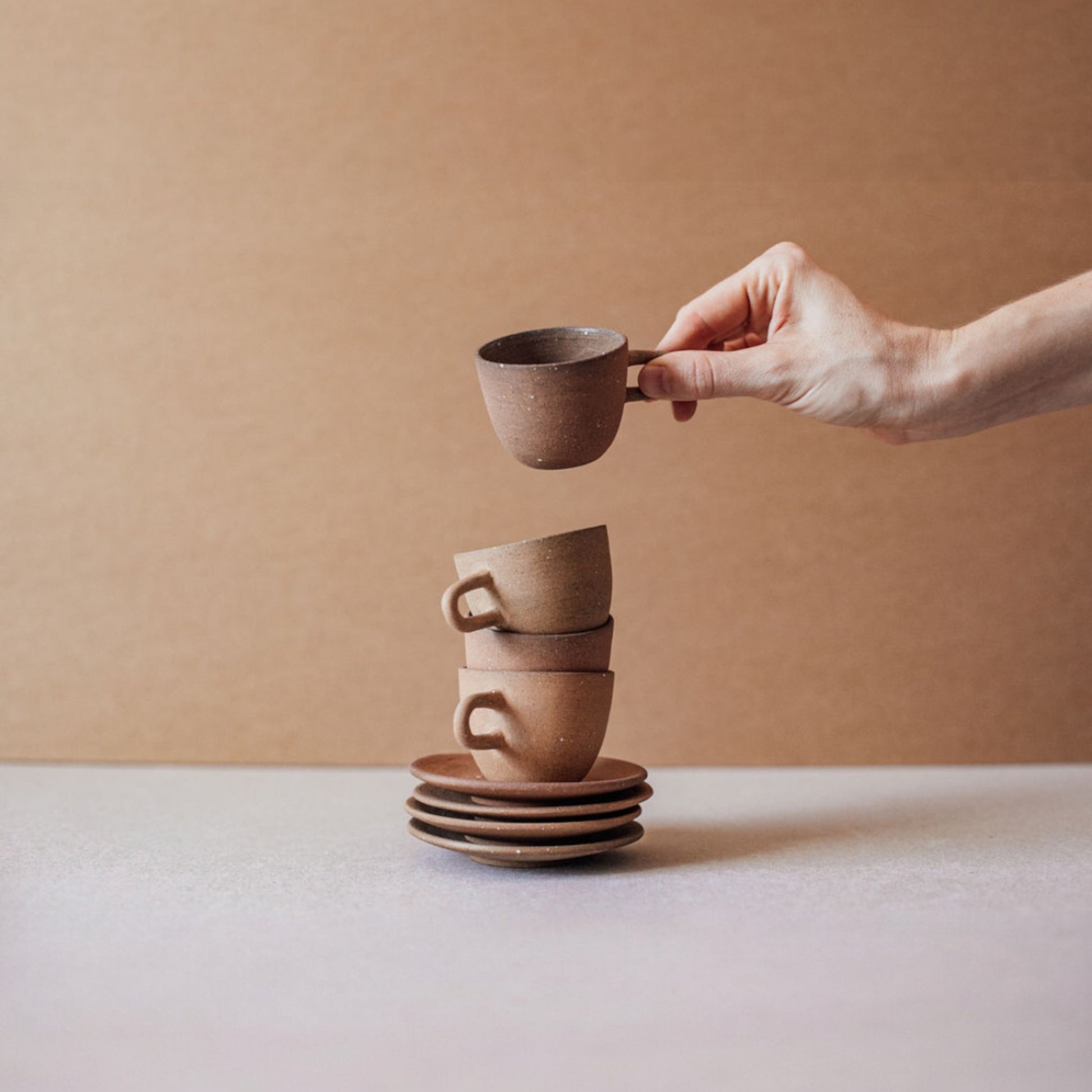 Hand placing terracotta espresso cup on stacked saucers