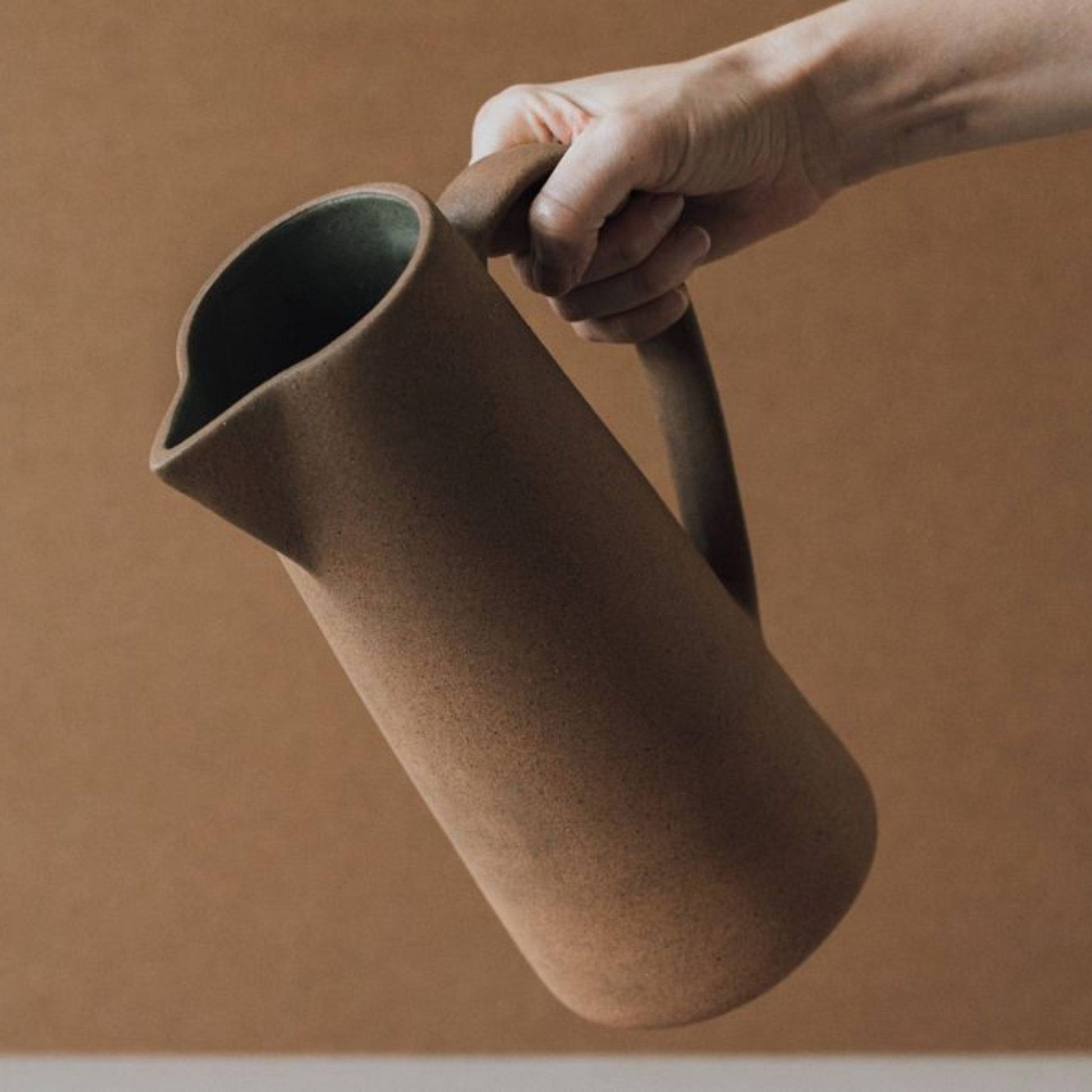 Tall terracotta clay jug held in hand showing scale and natural texture