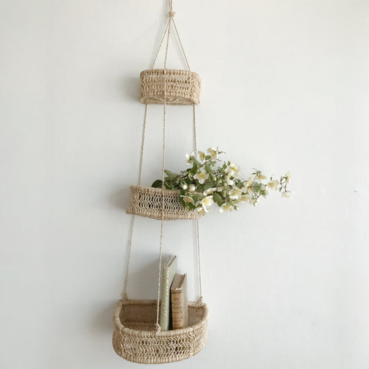 Handwoven three-tier jonote hanging basket with plants, displayed on a white wall.