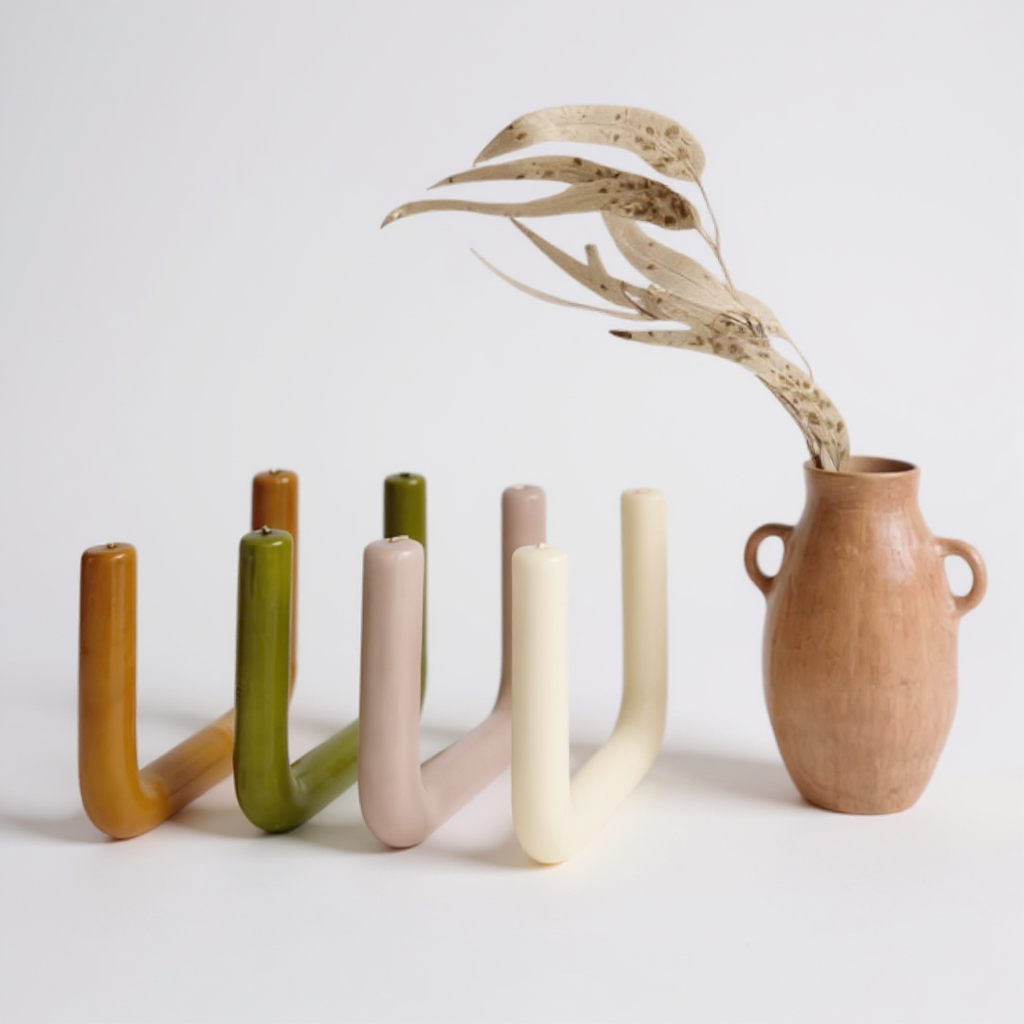 U-shaped handmade beeswax candles in assorted earthy colors displayed beside a terracotta vase on a white background.