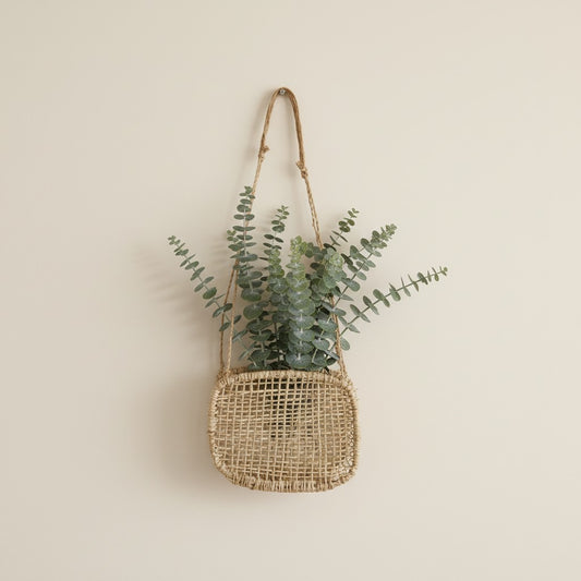 Woven square jonote wall basket with eucalyptus on a beige background