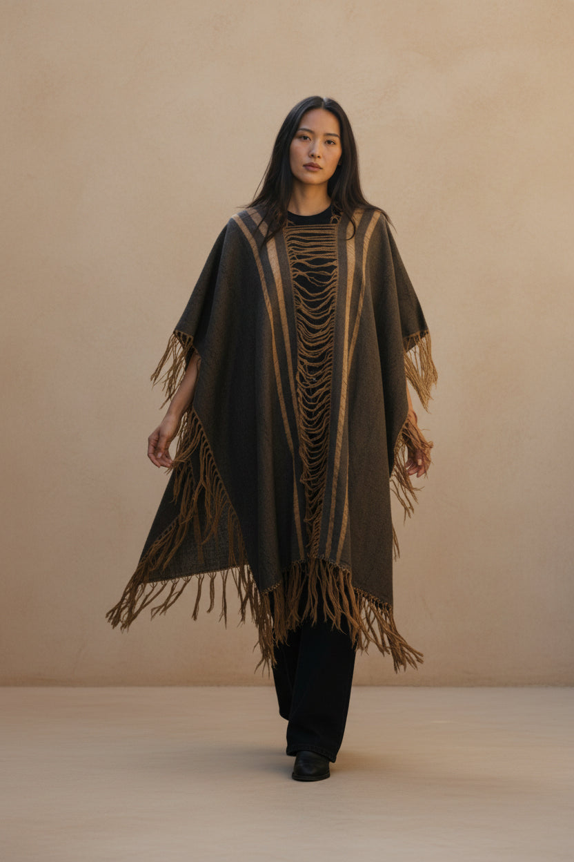 Model wearing a handwoven green and ivory Mexican poncho with geometric pattern, styled over neutral trousers against a warm textured wall