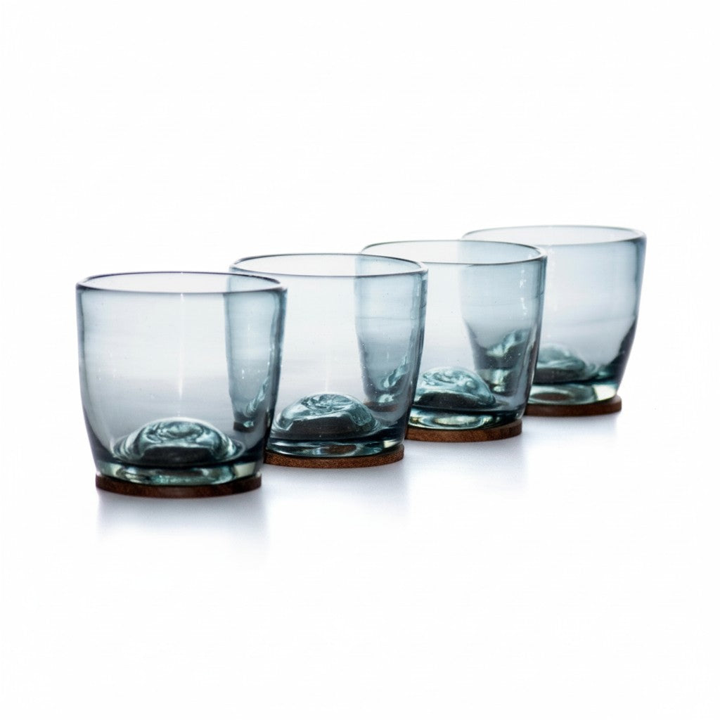Set of four smoky blue glass tumblers with round wooden bases on a white background.