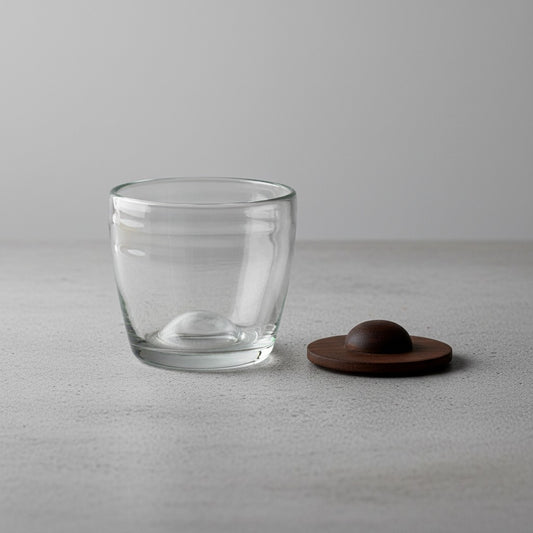 Clear hand-blown glass tumbler with its parota wood coaster on a light gray surface.
